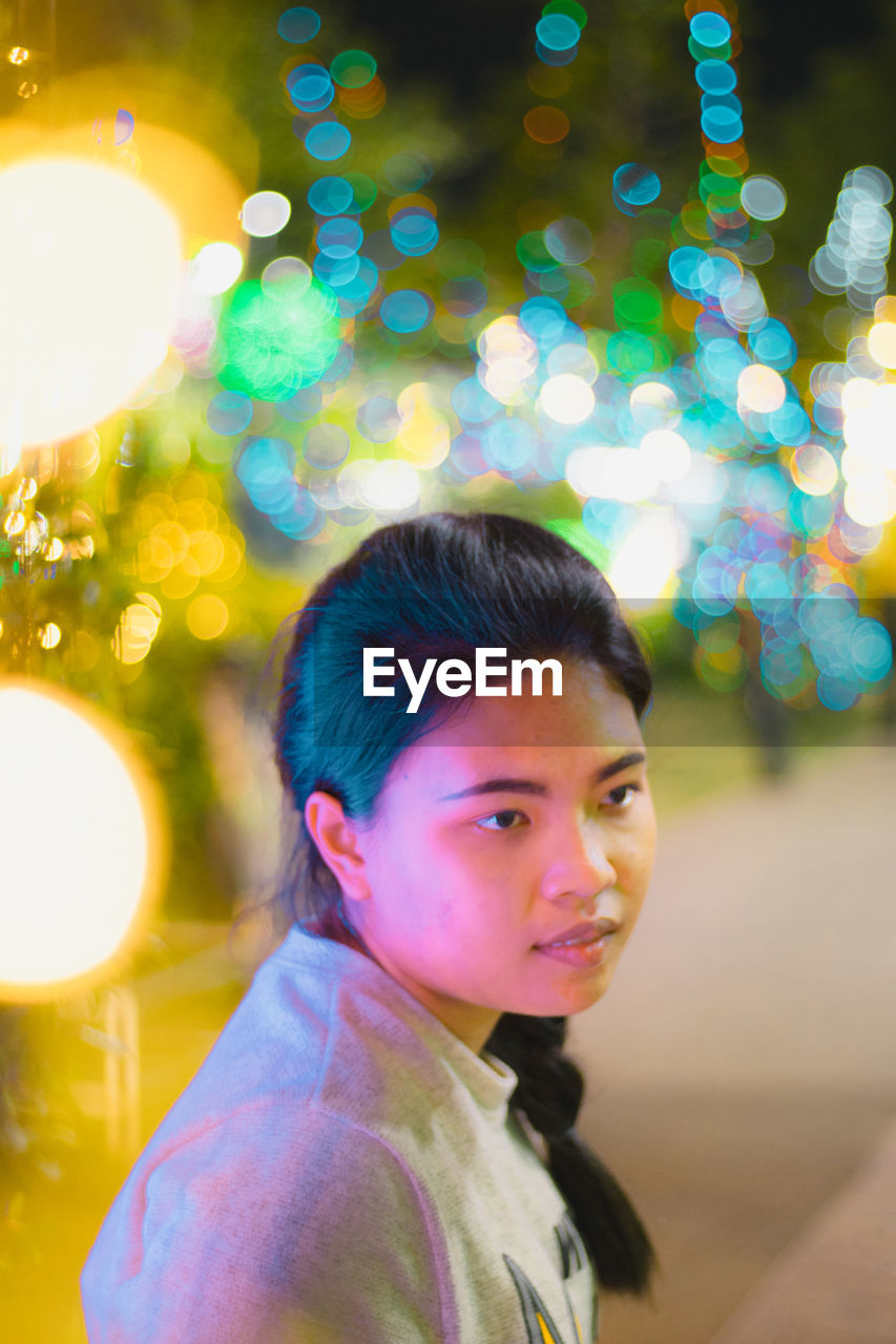 PORTRAIT OF WOMAN LOOKING AT ILLUMINATED LIGHTS