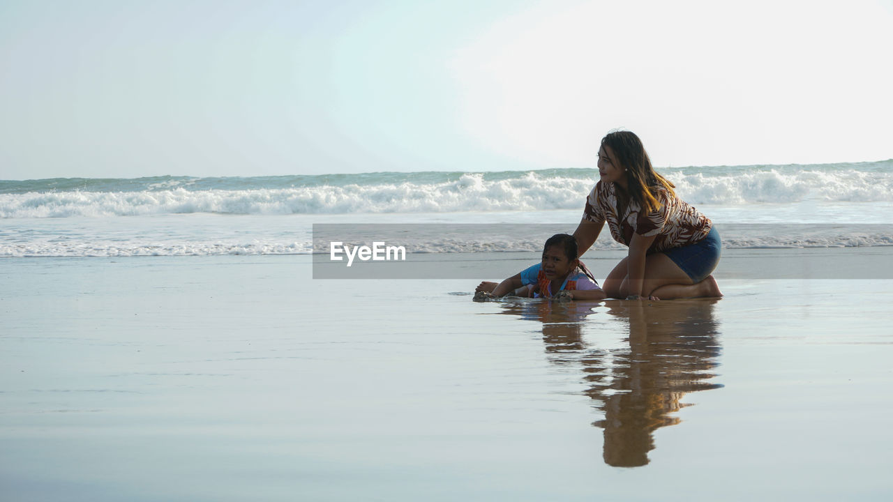 Woman sitting on shore at beach against sky