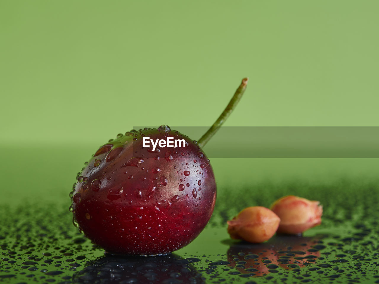Cherry with two bones on a green wet background with water drops.