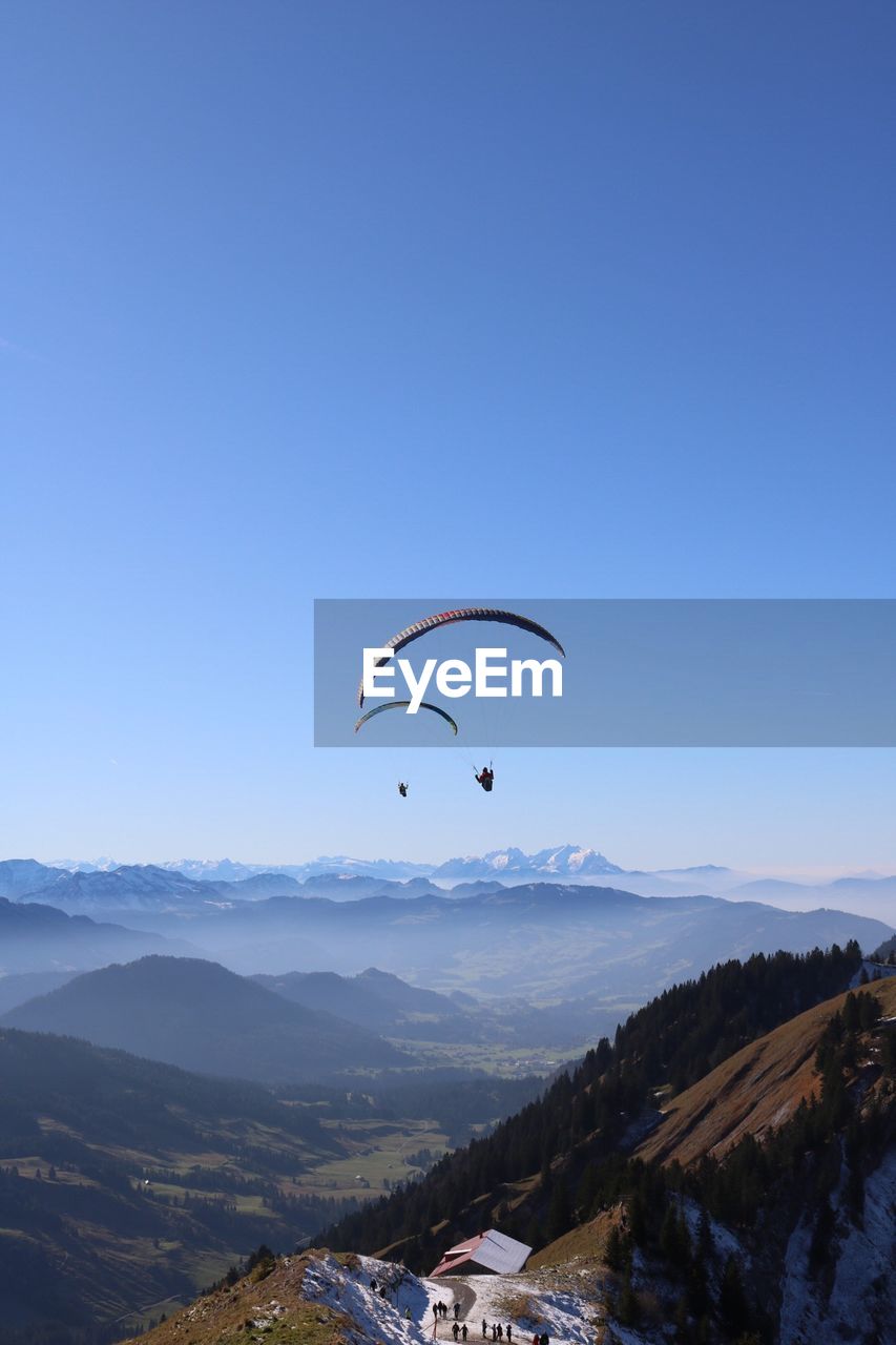 People paragliding against clear blue sky