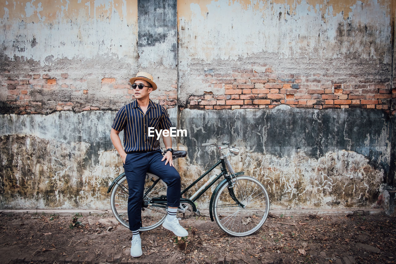 Man sitting on bicycle against wall in city