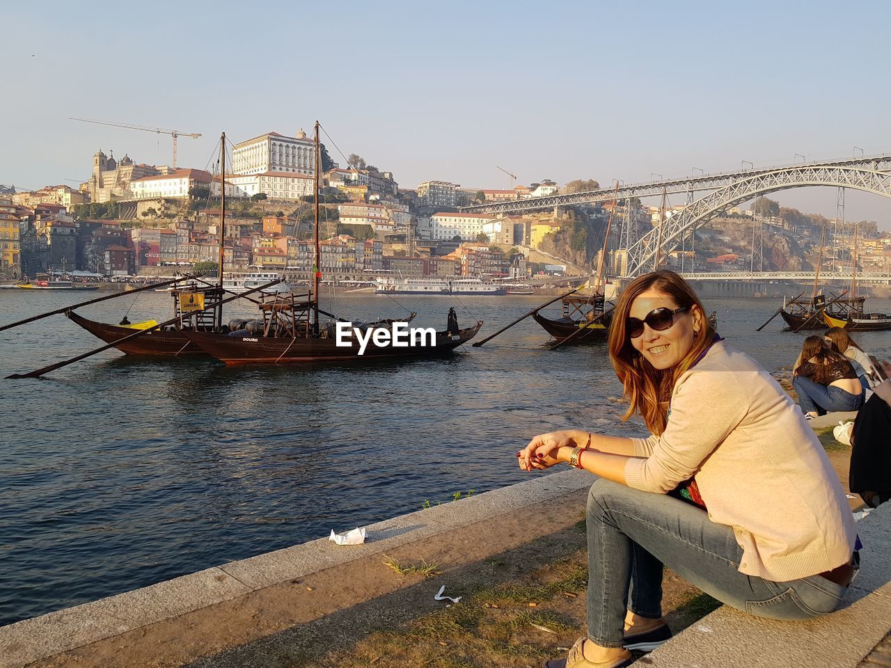 Woman sitting on bridge over river in city against clear sky