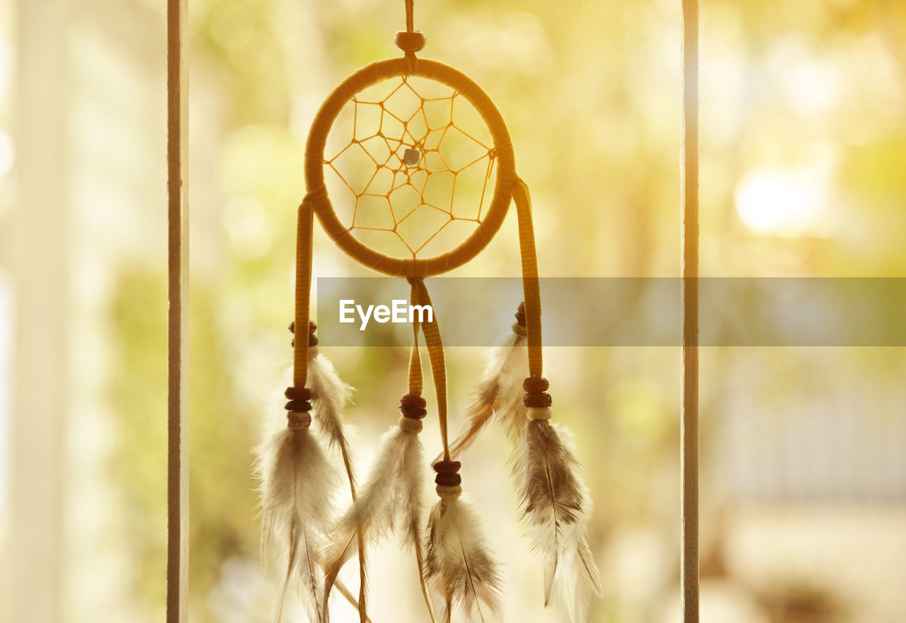 Close-up of dreamcatcher hanging at window against blurred background