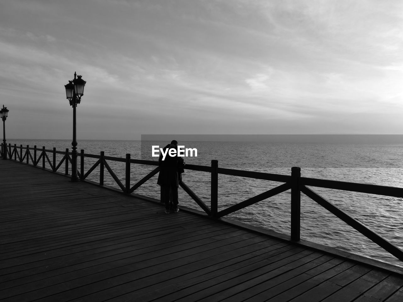 MAN STANDING BY RAILING AGAINST SEA