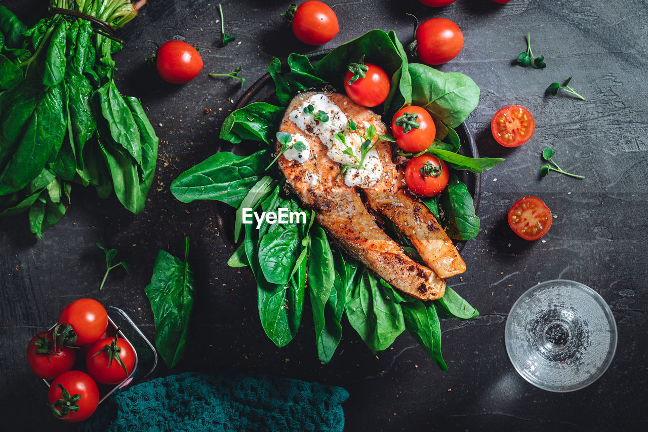 A plate with fresh green raw spinach and fried wild salmon, tomatoes and cream cheese sauce 