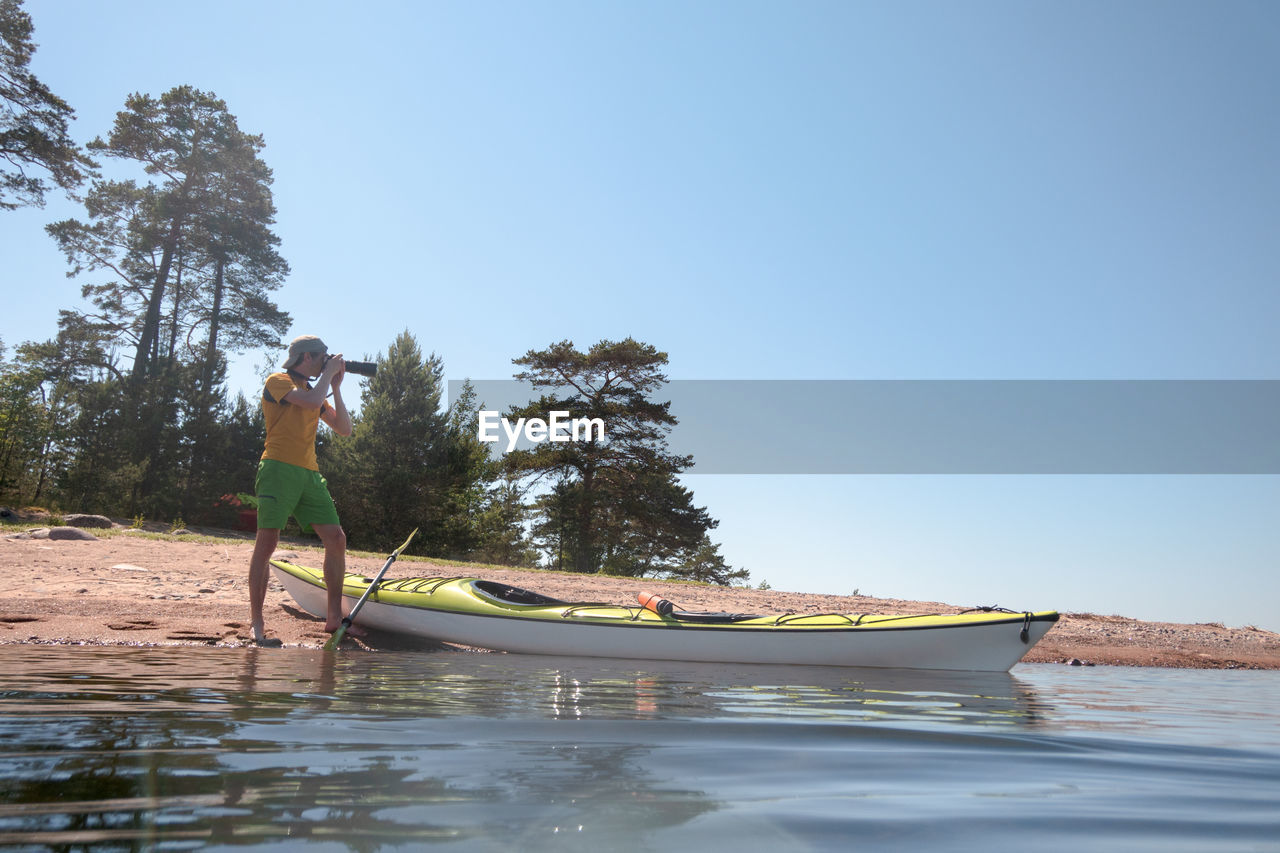 Naturalist photographer at work on the shore in a picturesque location. next to him is a kayak