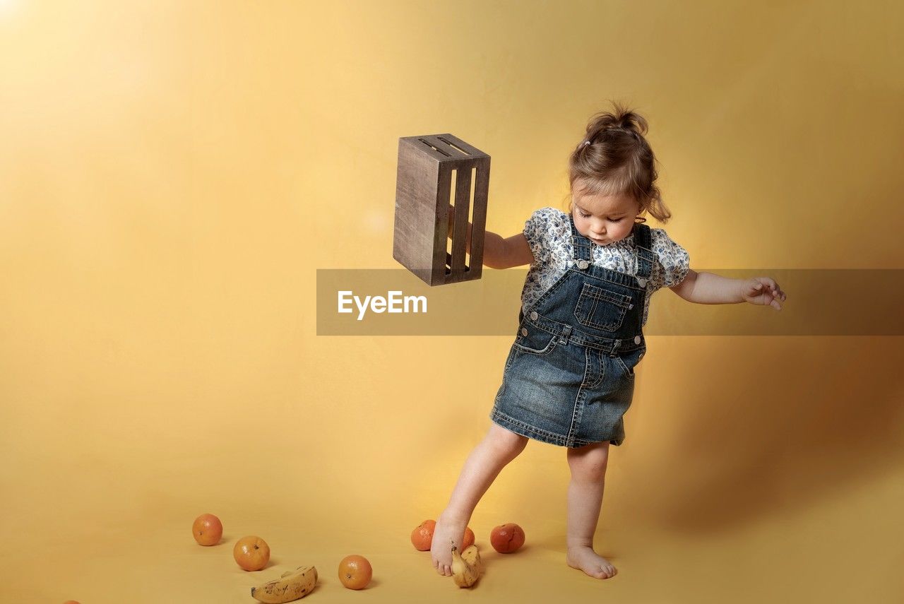 childhood, child, full length, one person, indoors, yellow, colored background, fun, toddler, casual clothing, person, cute, emotion, studio shot, female, happiness, toy, copy space, women, holding, innocence, jumping, mid-air, standing, barefoot, smiling, motion