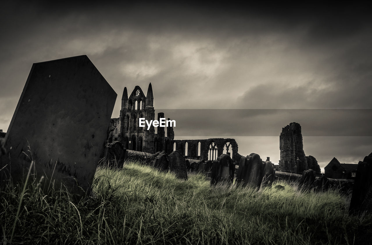 Low angle view of abandoned cemetery against cloudy sky at dusk