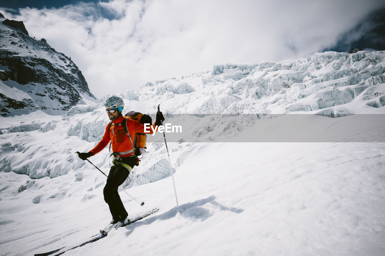 Man skiing on snow covered mountain against cloudy sky