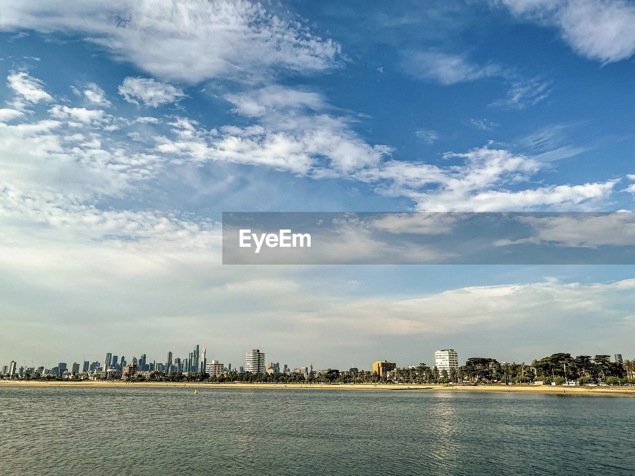 Distant view of st. kilda beachfront with buildings under blue sky with clouds and sea.