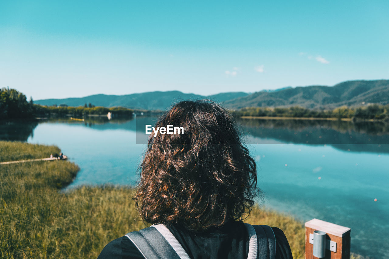 Girl sitting on the edge of banyoles lake on a sunny day with the landscape reflected in the water