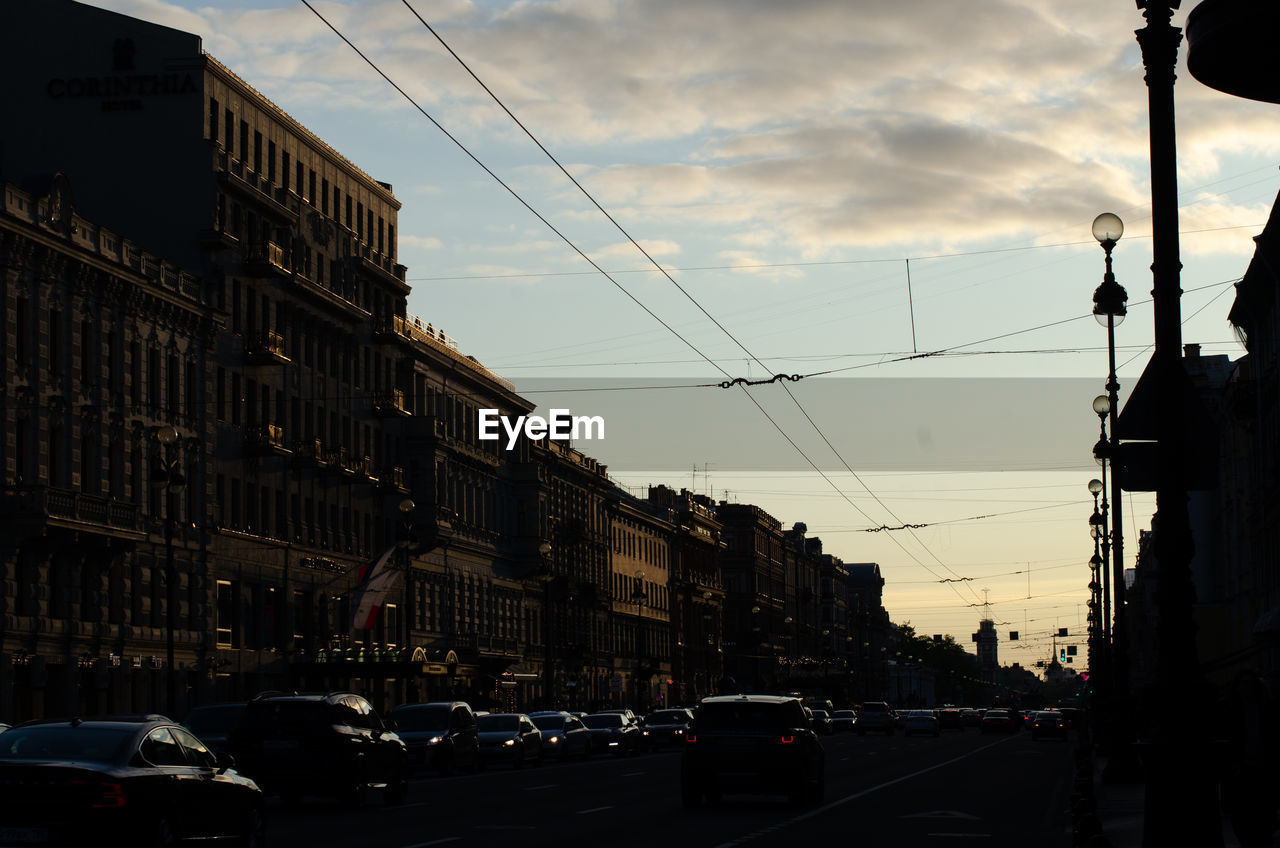 TRAFFIC ON ROAD BY BUILDINGS AGAINST SKY