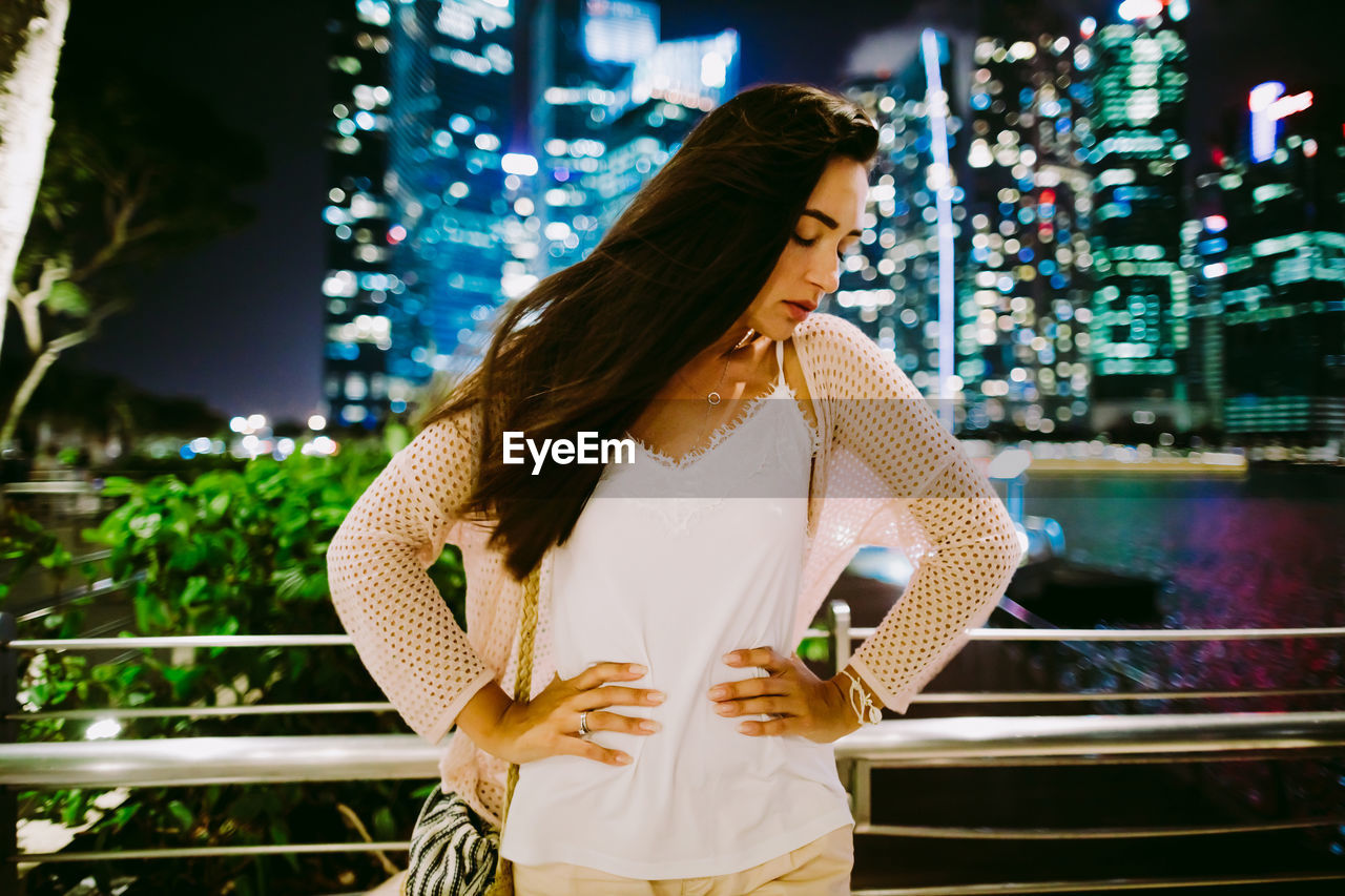 Woman with hand on hip standing in city at night