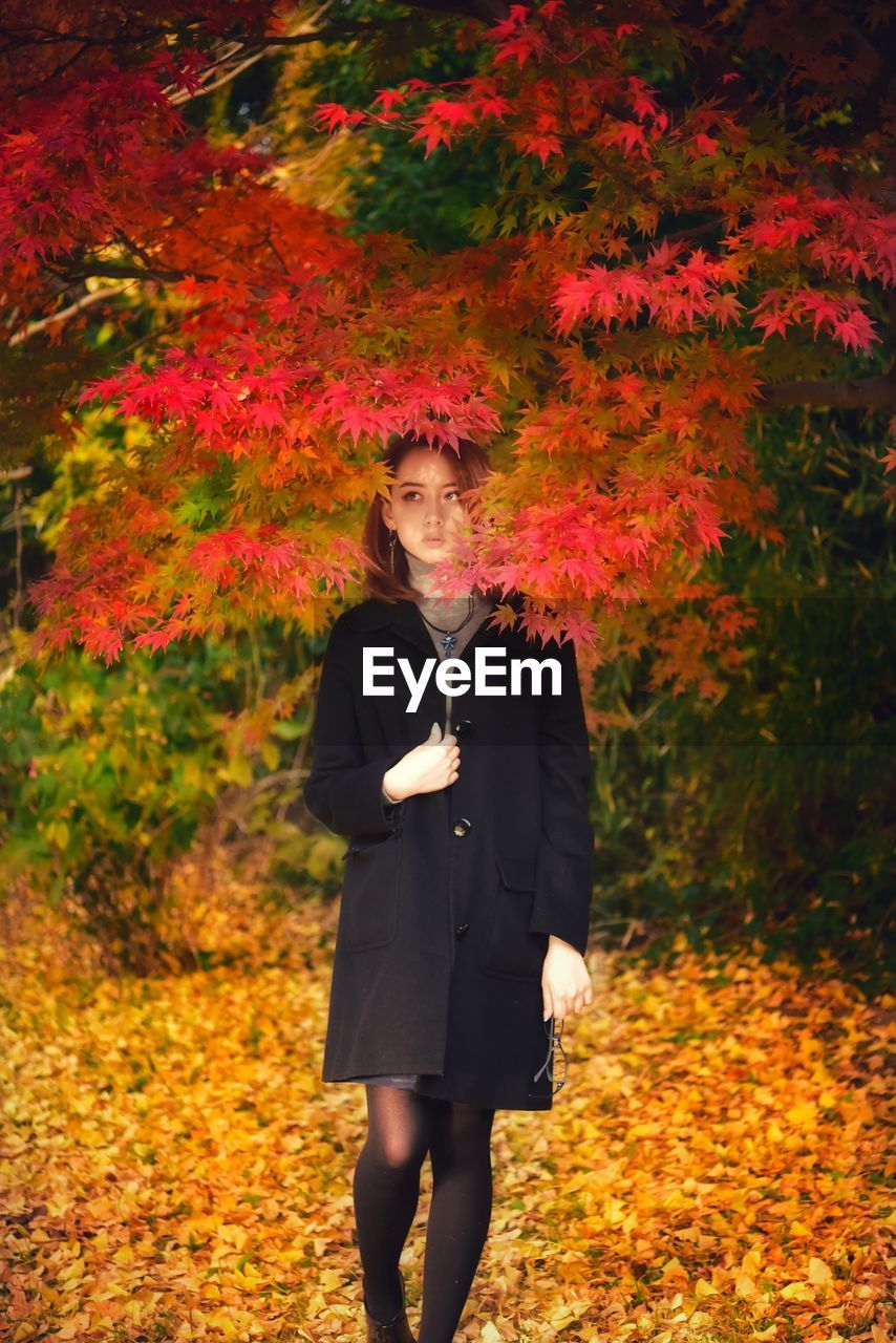 Full length of young woman standing by plants during autumn