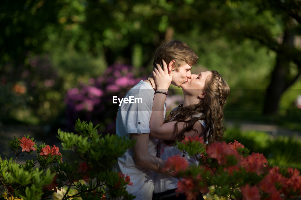 Side view of couple kissing while standing amidst flowers at park