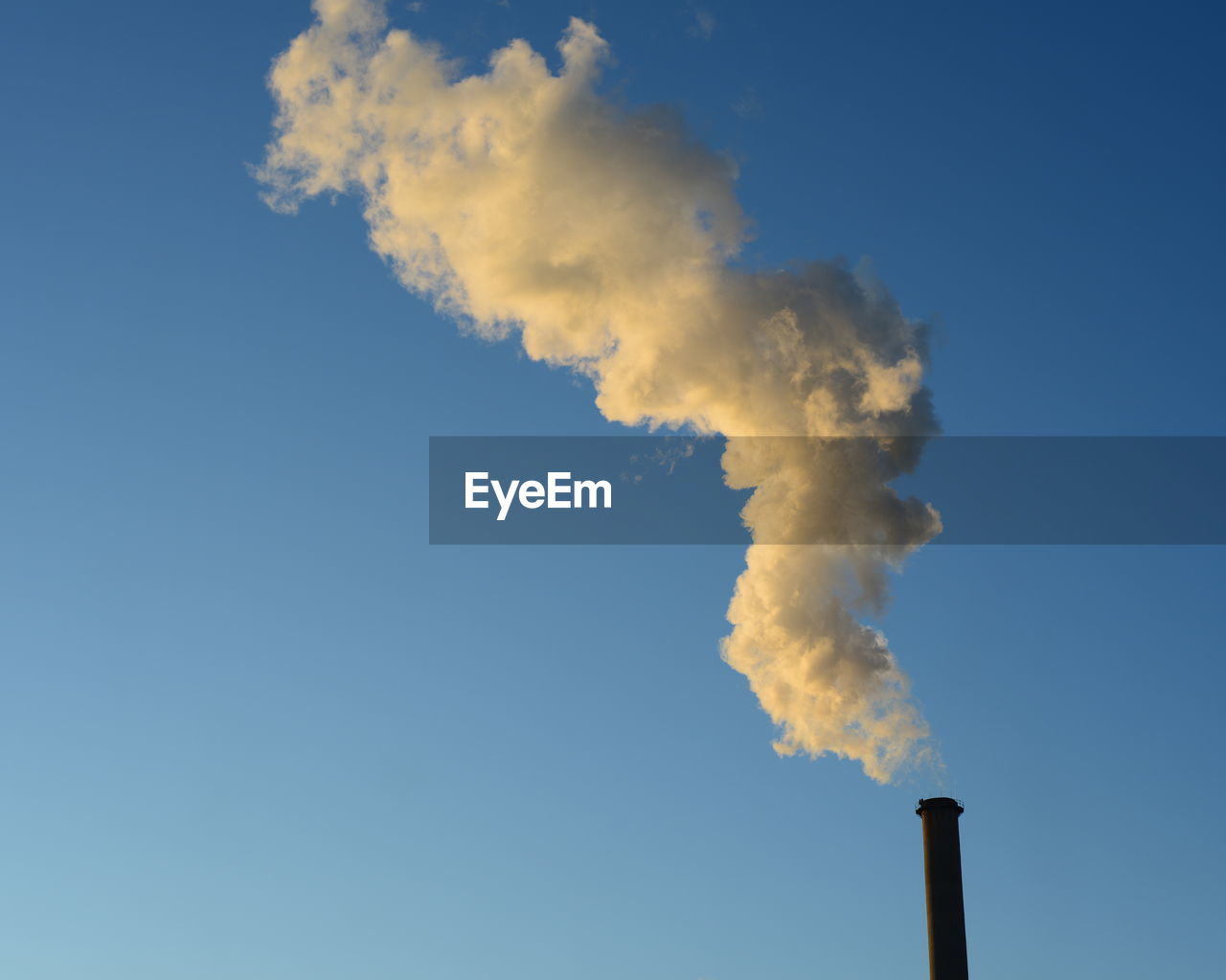 Low angle view of smoke emitting from chimney against blue sky