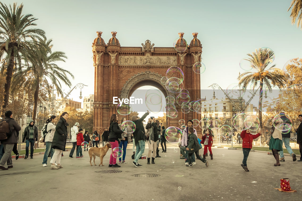 People playing with soap bubbles at arc de triomf against sky