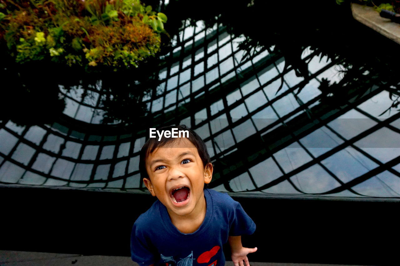 Close-up portrait of boy shouting while standing against pond