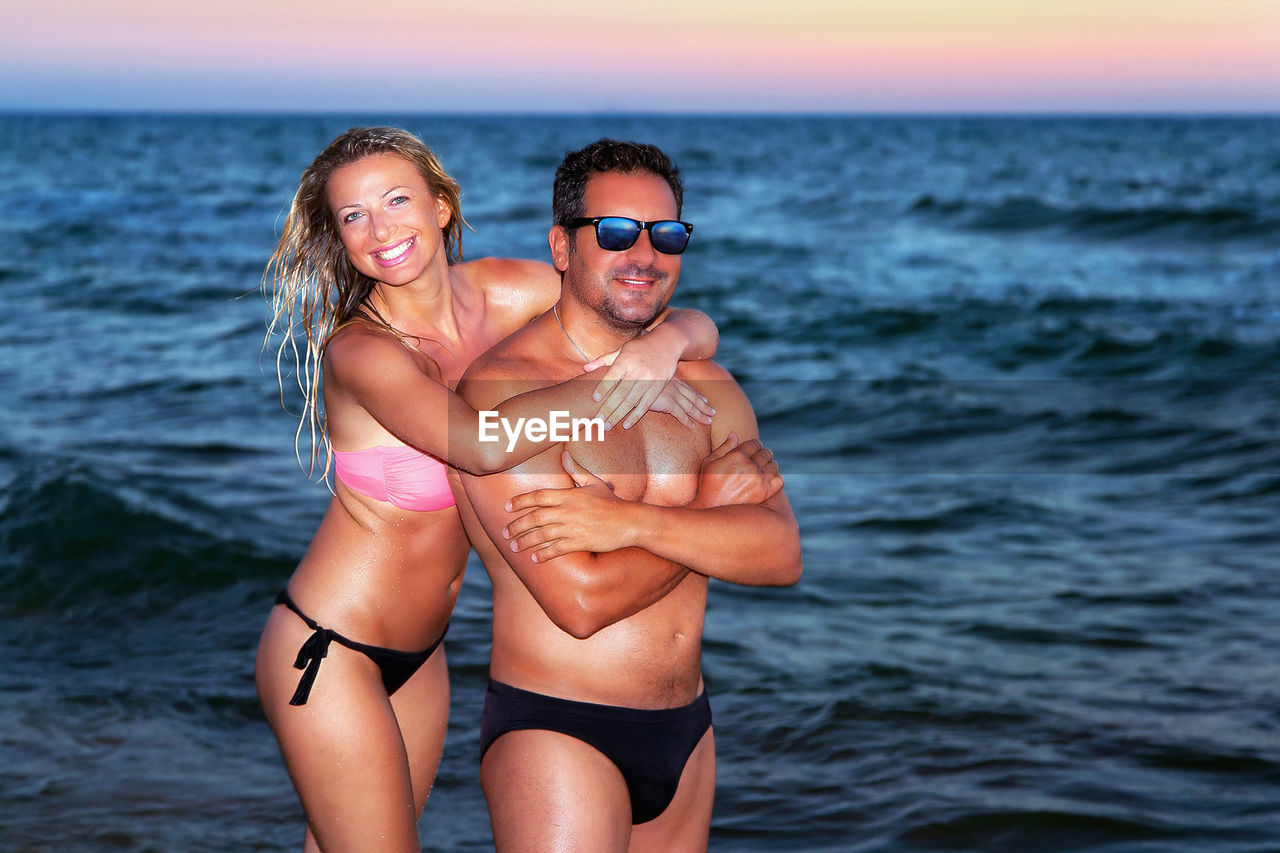 Couple woman and a man portraits at sunset at sea while they embrace