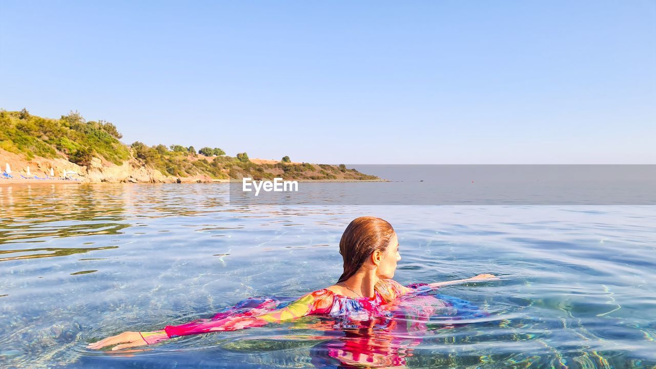 Woman swimming in sea against clear sky