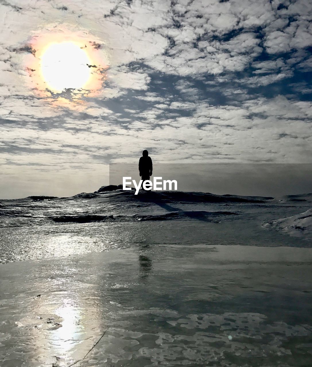 MAN WALKING ON WET SHORE AGAINST SKY