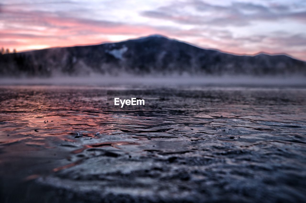 Scenic view of frozen lake and mountain against sky during sunrise