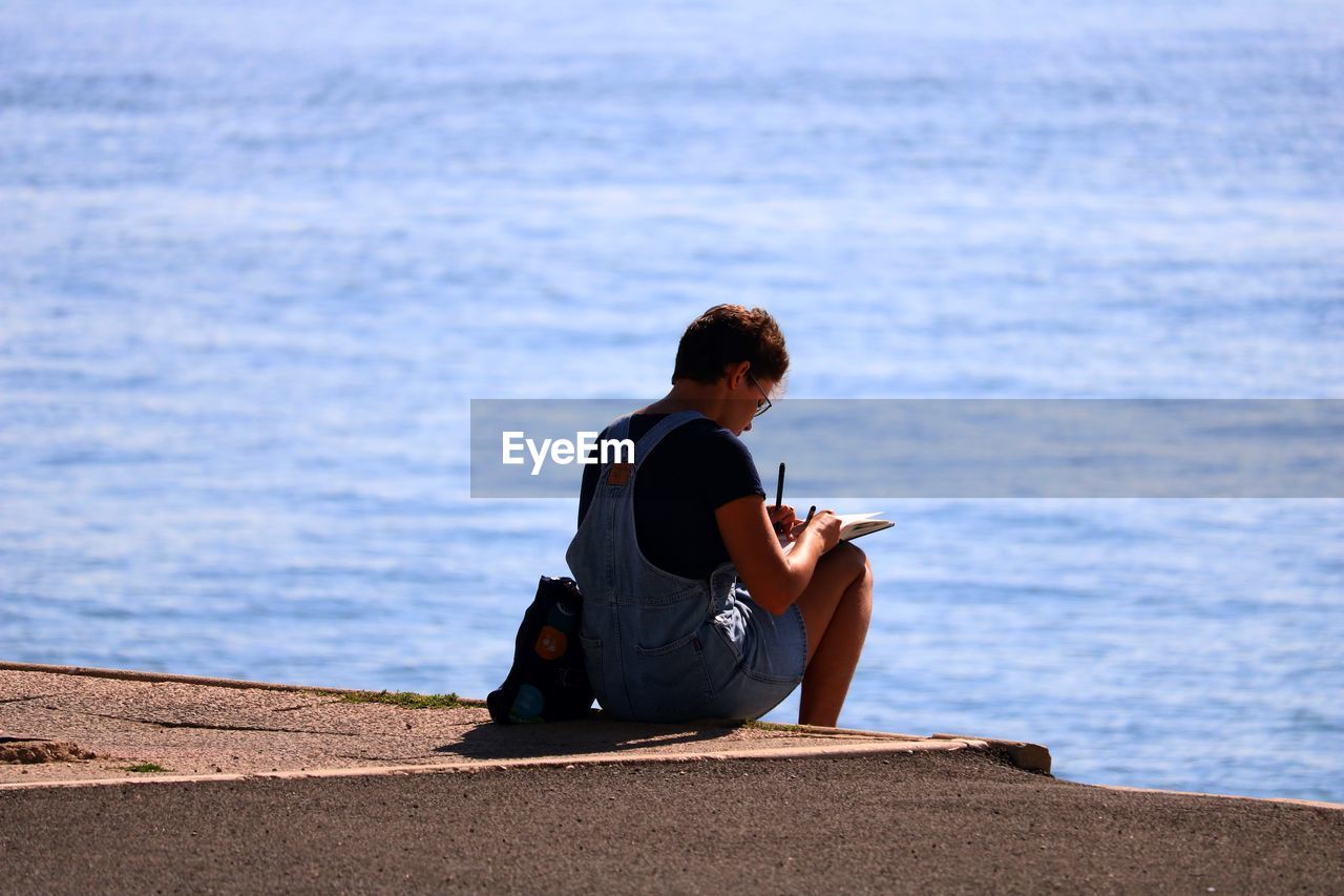 MAN USING MOBILE PHONE WHILE SITTING ON RETAINING WALL