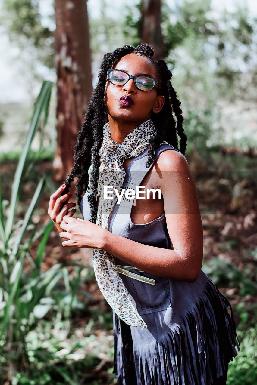 Portrait of young woman wearing eyeglasses standing against plants