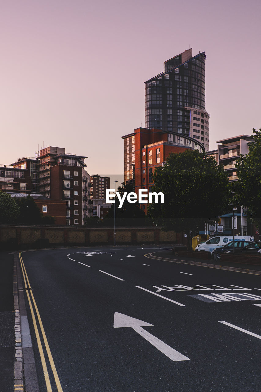 Diminishing perspective of road by buildings against clear sky during sunset