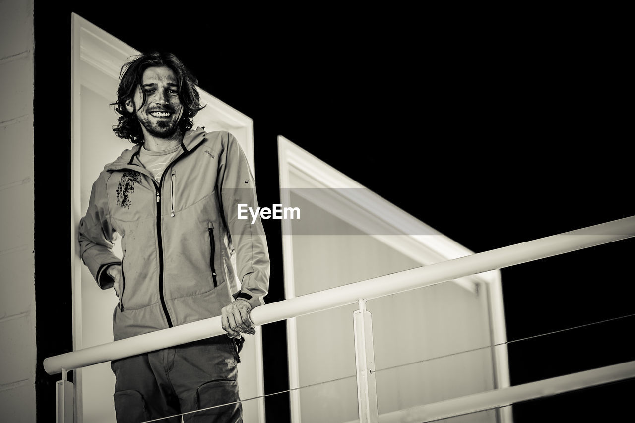 PORTRAIT OF MAN STANDING AGAINST RAILING