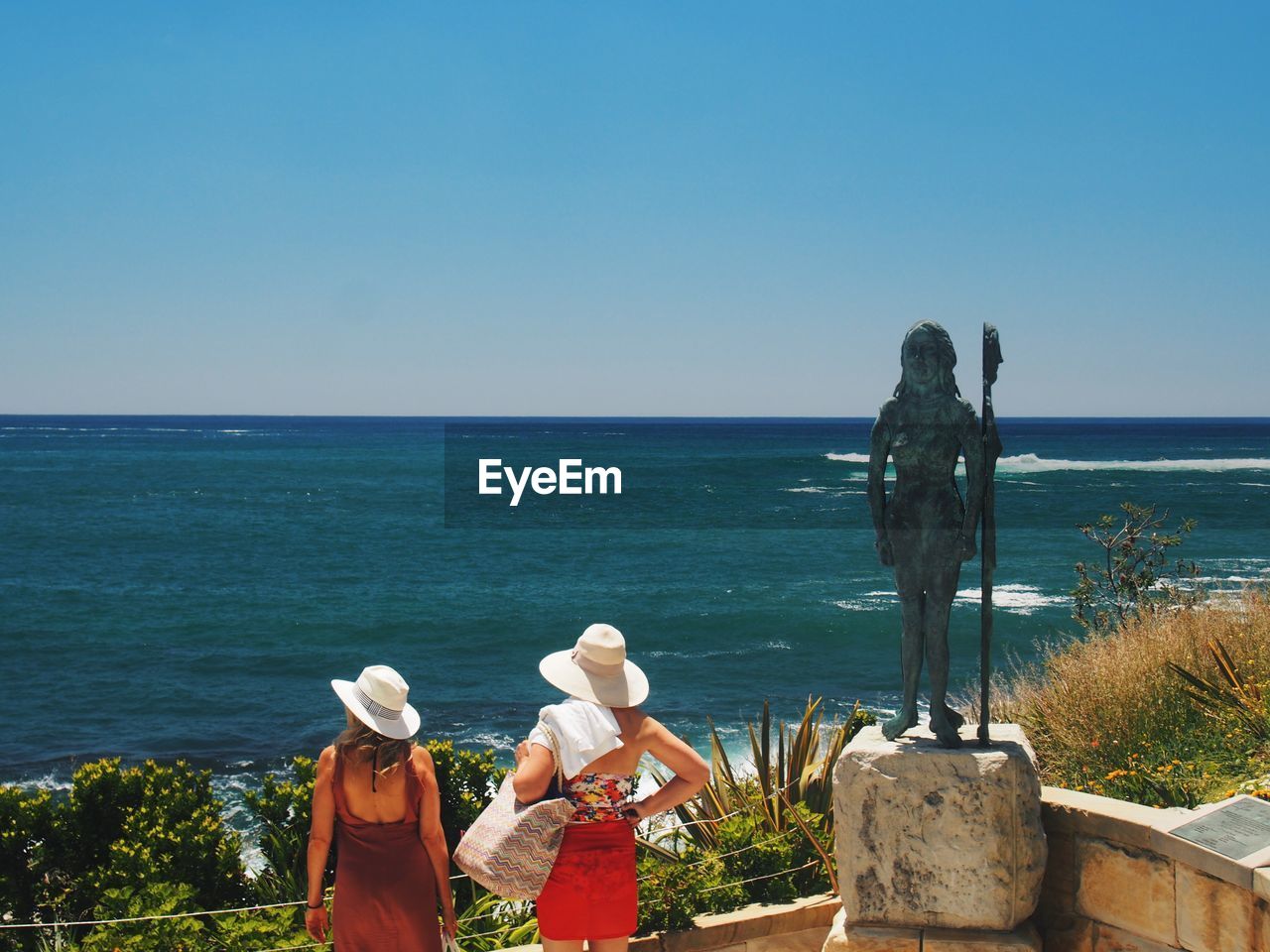 Rear view of women looking at sea against clear sky during summer