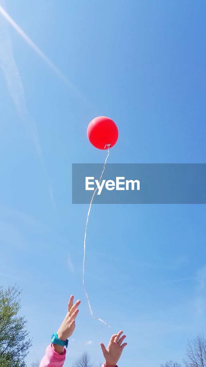 Low angle view of girl reaching balloon flying against blue sky