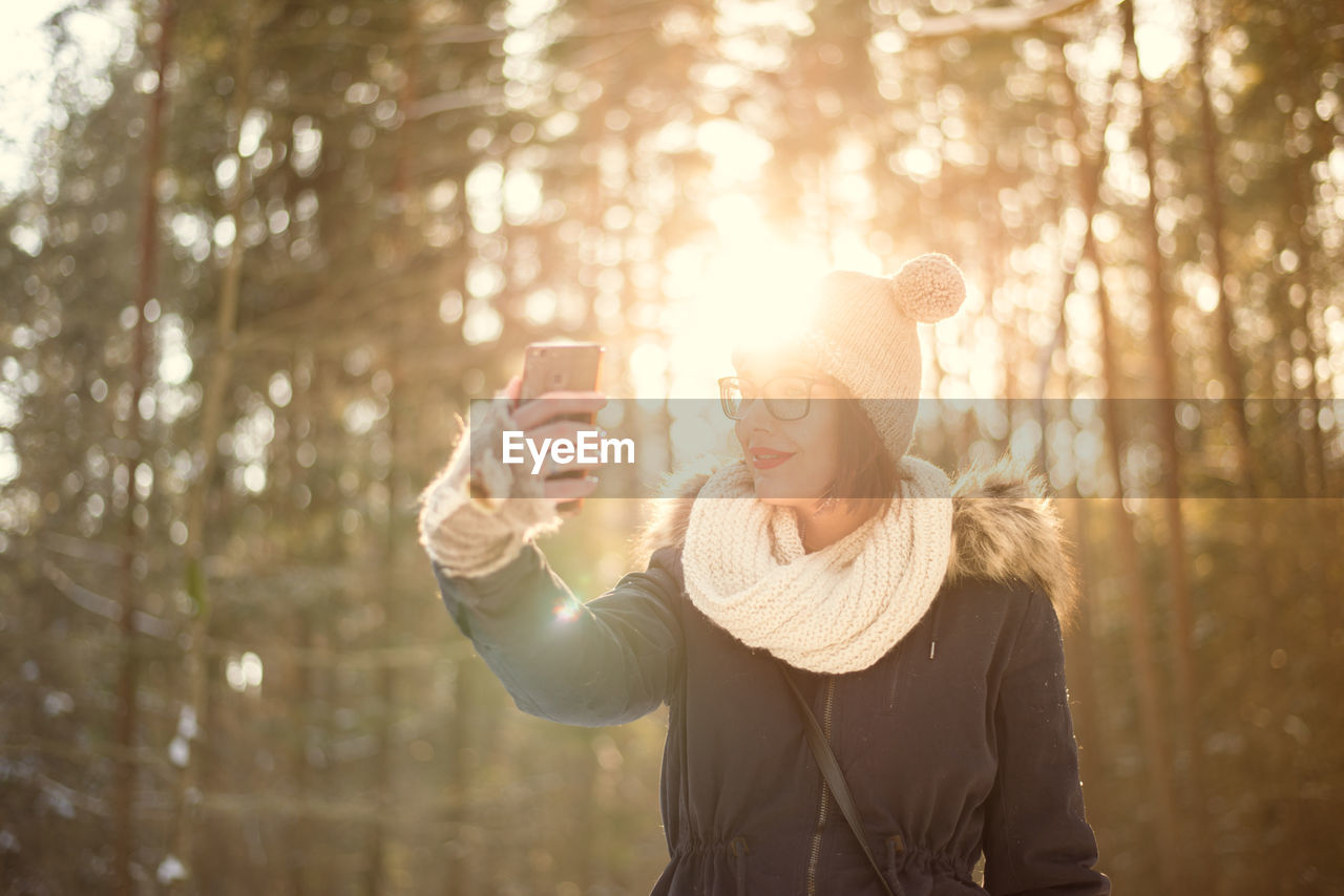 Young woman photographing taking selfie with mobile phone on snow covered field