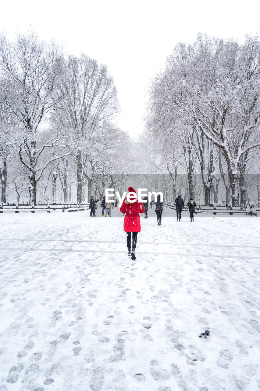 REAR VIEW OF WOMAN WALKING ON SNOW COVERED FIELD