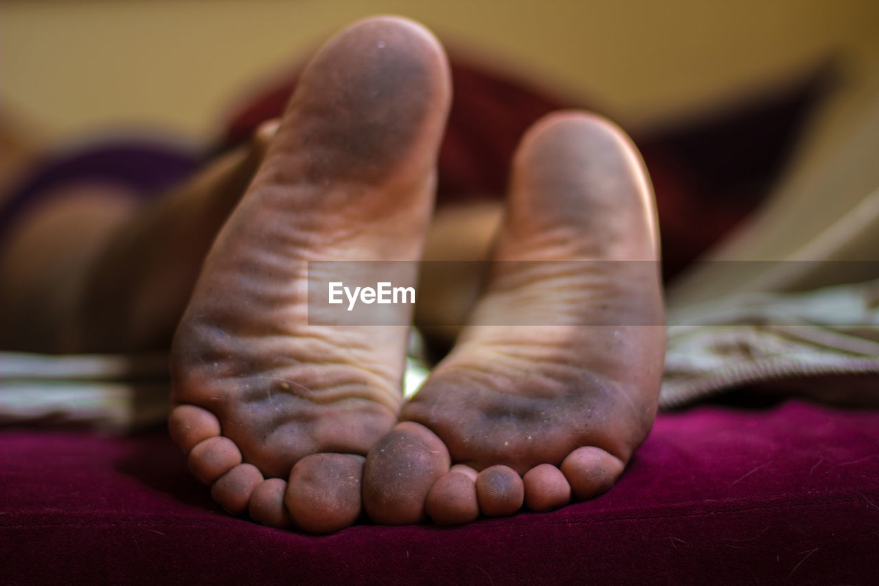 Close-up of messy feet of person lying in bed at home