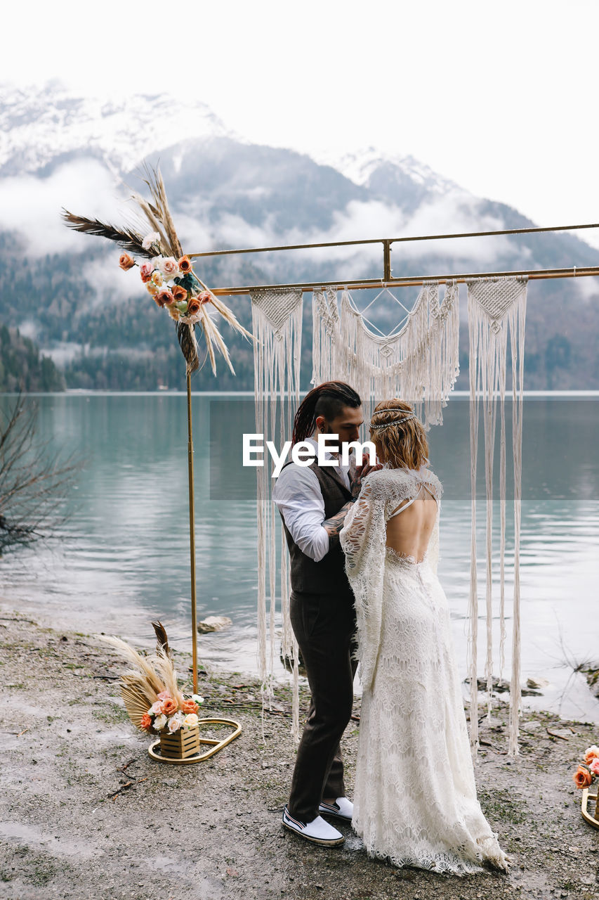 Happy newlyweds in love a man and a woman in wedding clothes embrace on the shore of the lake