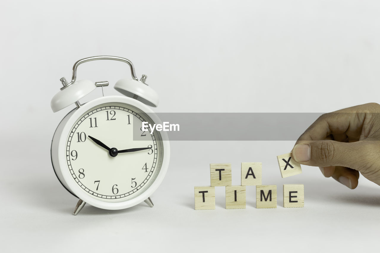 White alarm clock with handing tax wooden block cube on white background.