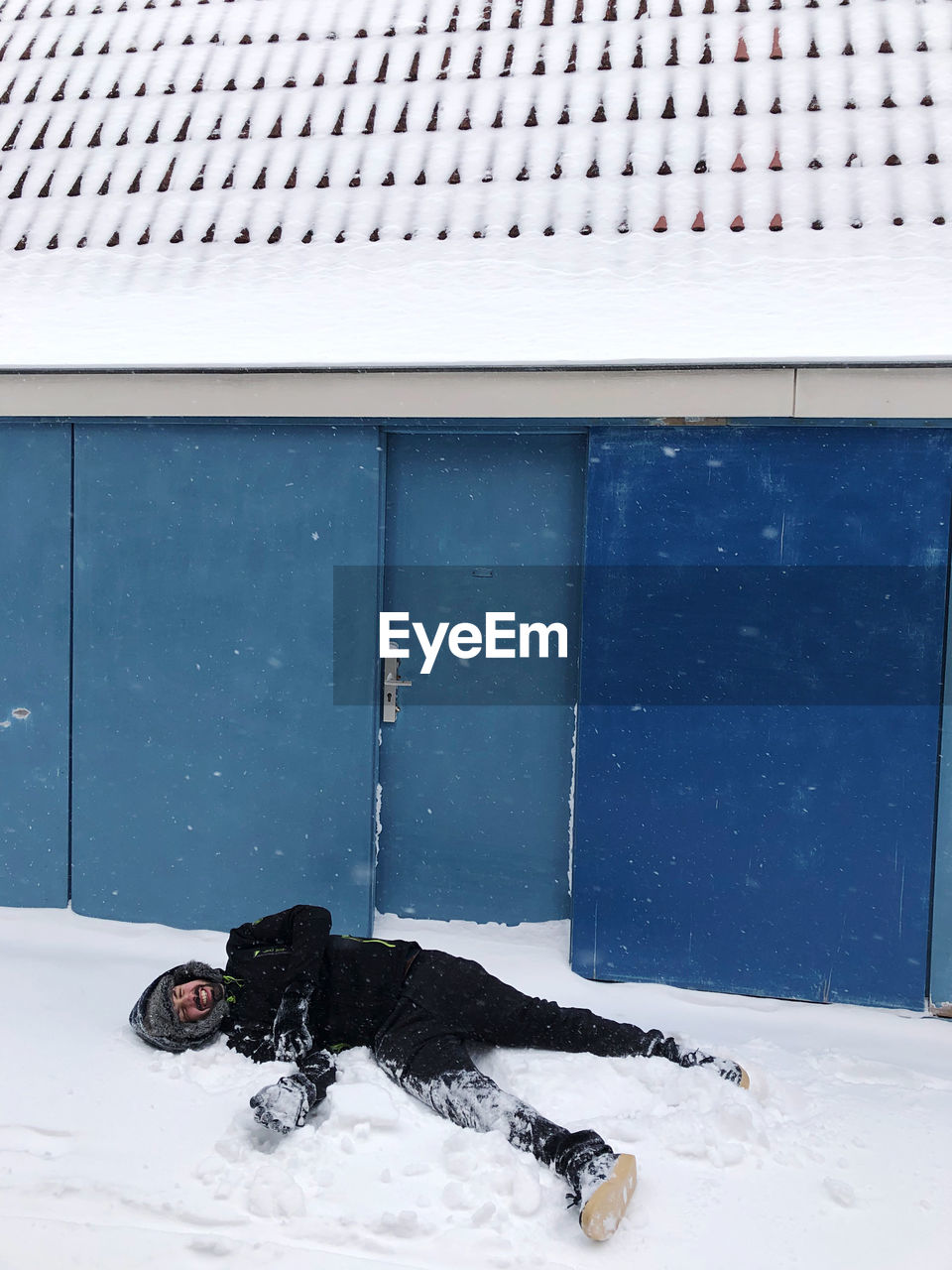 Man in the snow next to a blue building