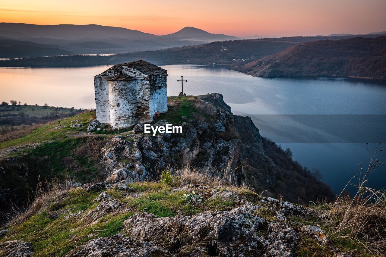 Scenic view of lake by mountain against sky during sunset