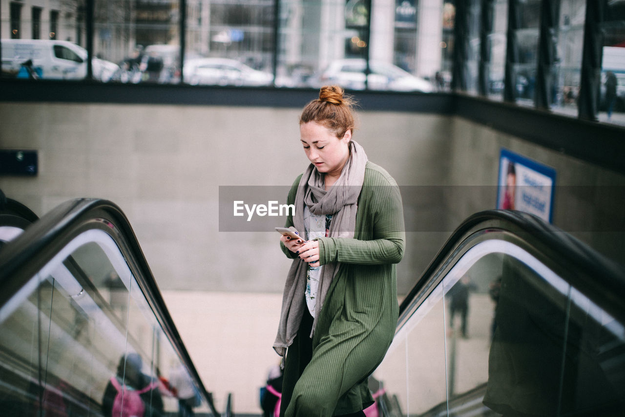 YOUNG WOMAN LOOKING AT CAMERA WHILE STANDING ON CITY