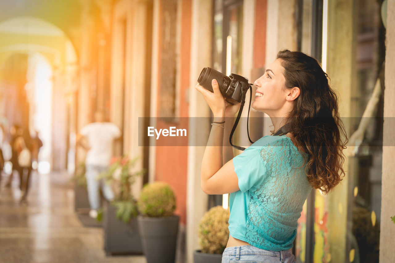 Smiling young woman photographing in city