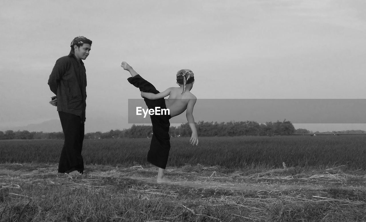 Man looking at son practicing martial arts on field