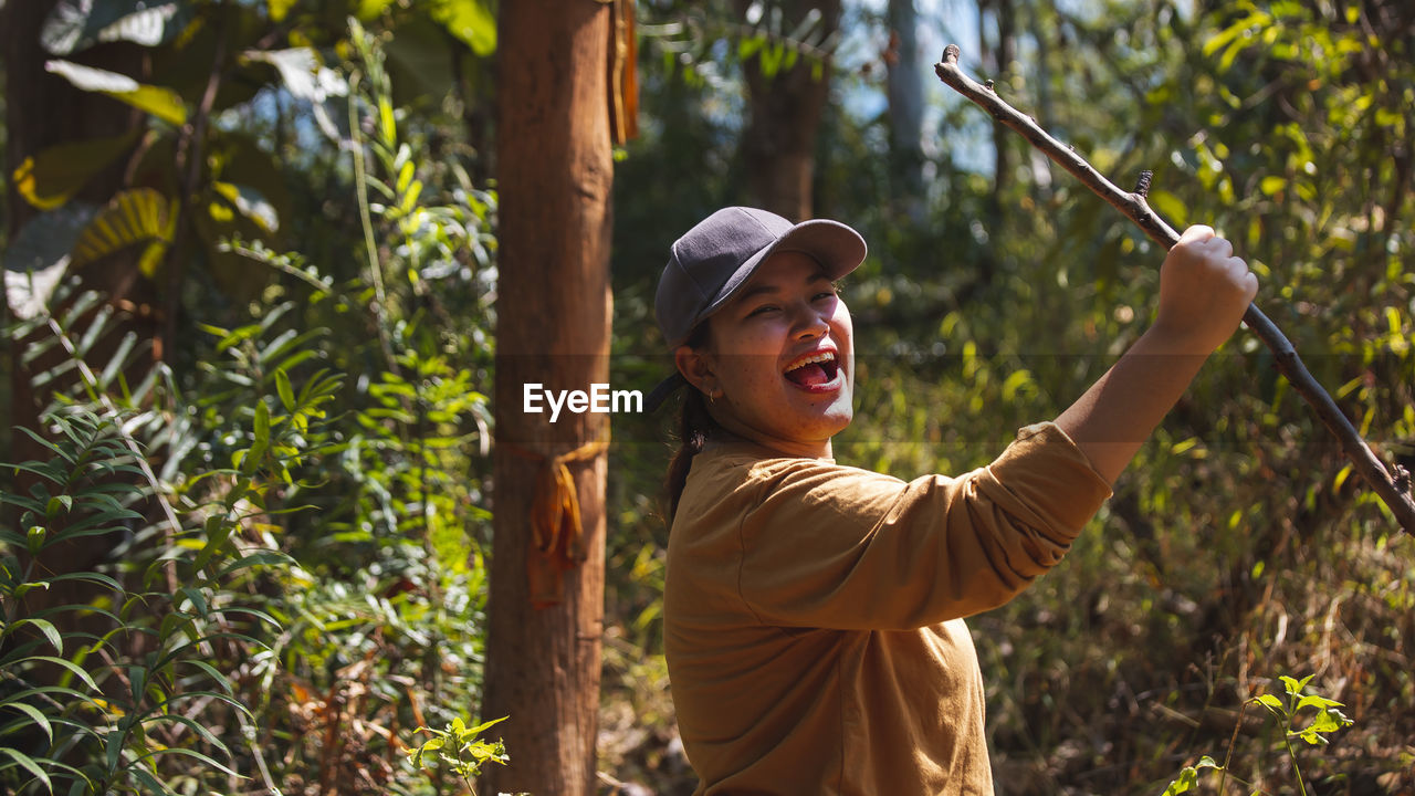 Happy young woman standing against plants