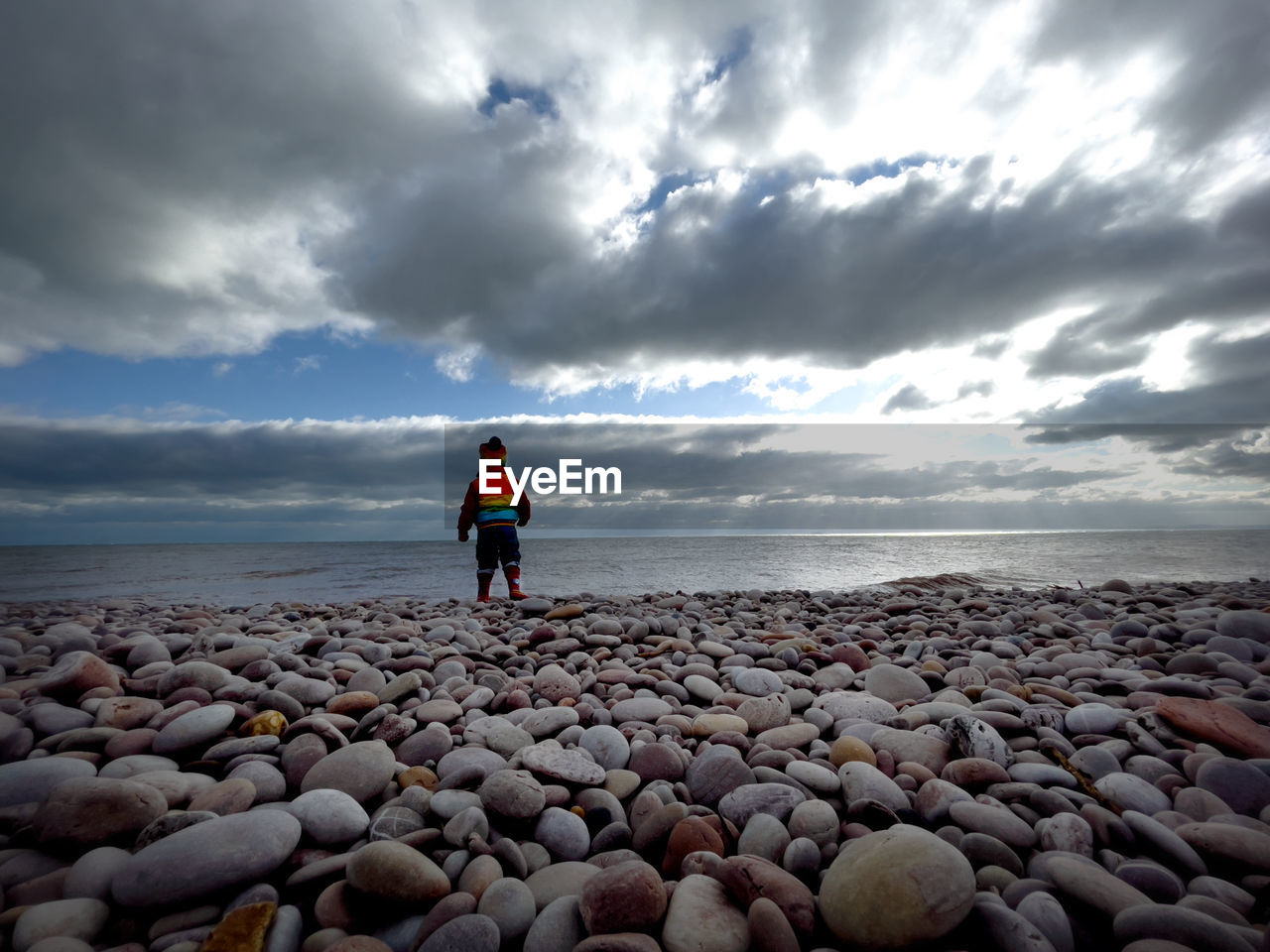 REAR VIEW OF PERSON STANDING AT BEACH