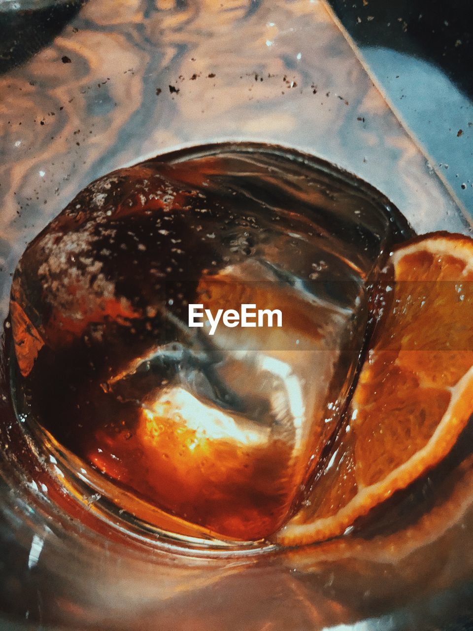A glass of whiskey with an ice cube and an orange slice