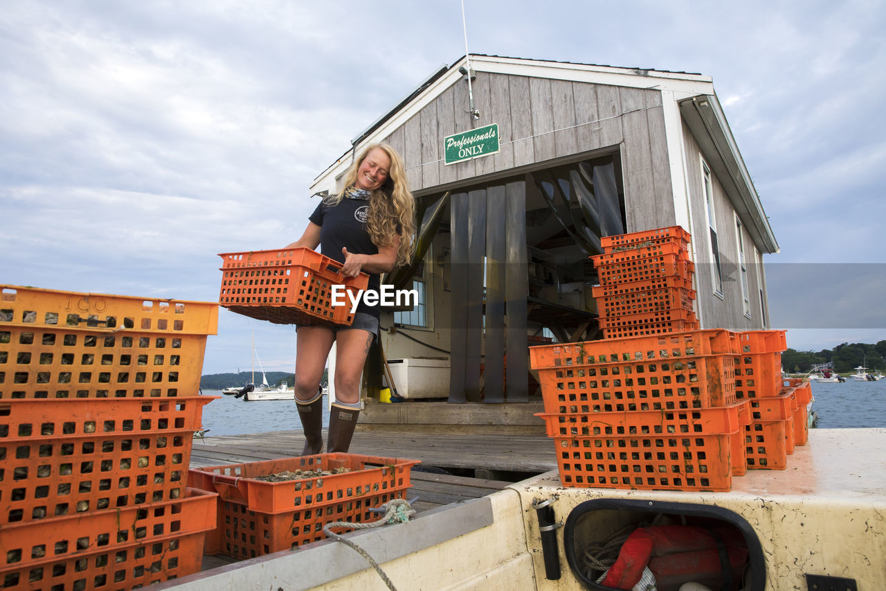 Female shellfish farmer carrying orange crates of oysters