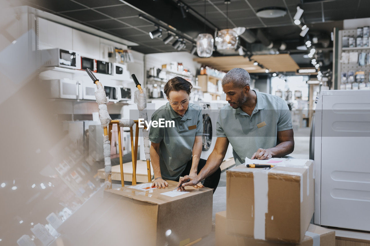 Multiracial male and female colleagues discussing over box while working in electronics store