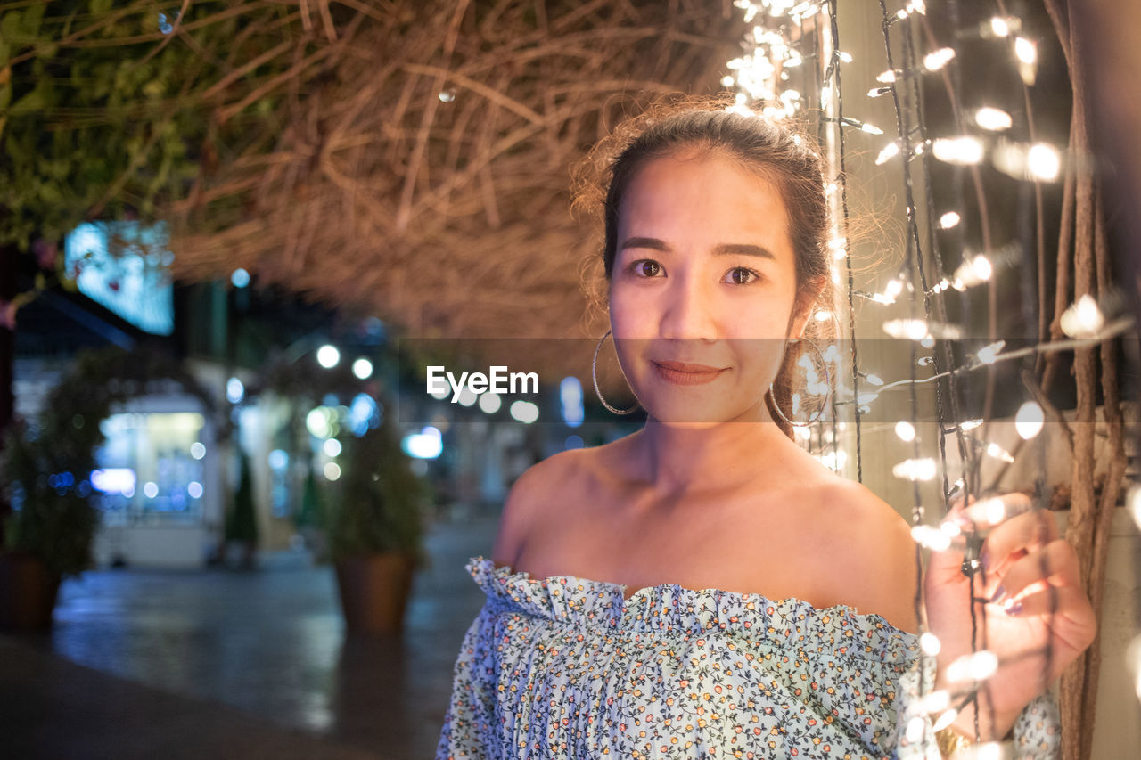 Portrait of smiling young woman holding illuminated lighting equipment