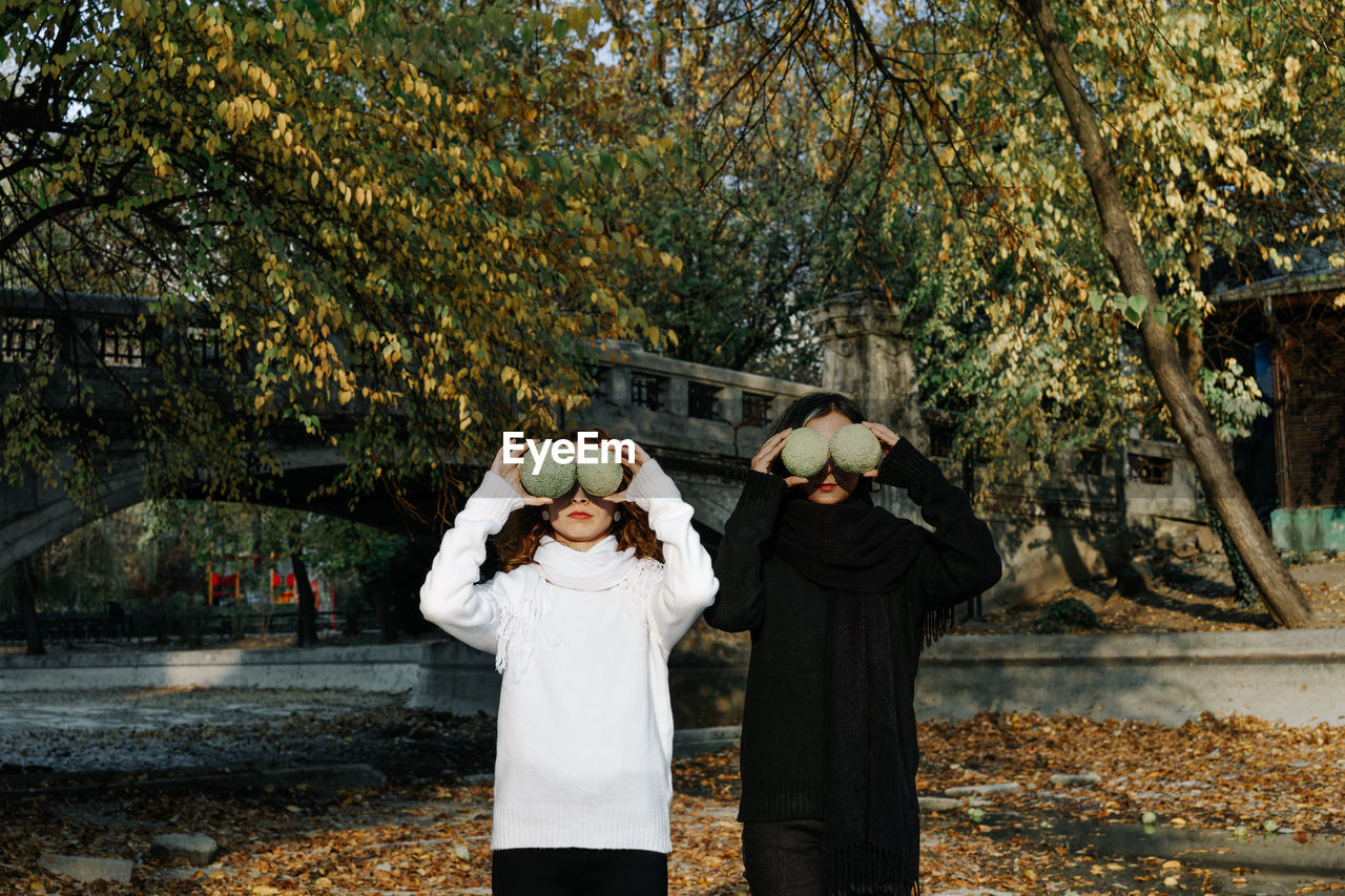 Lesbian couple holding fruits while standing against trees in park during autumn