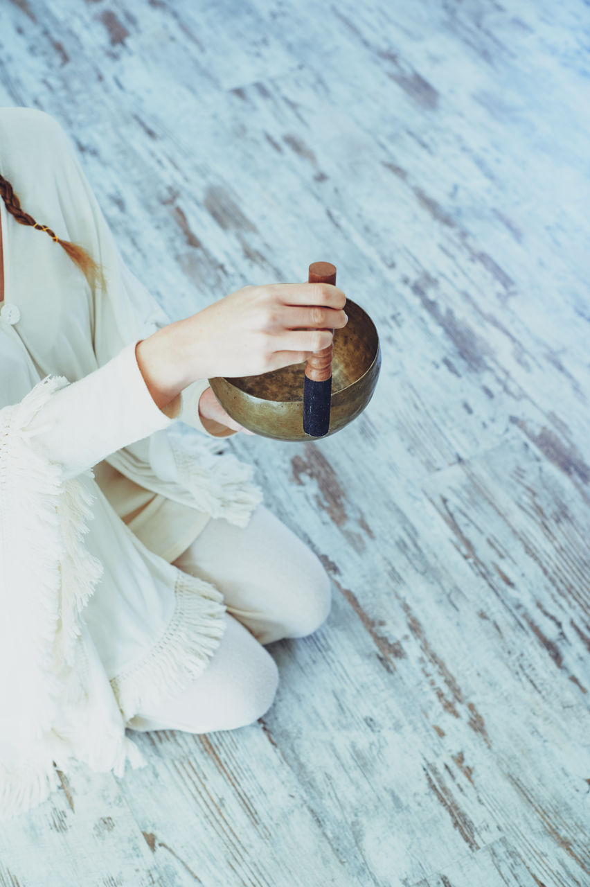 Crop woman playing singing bowl with wooden striker during spiritual practice